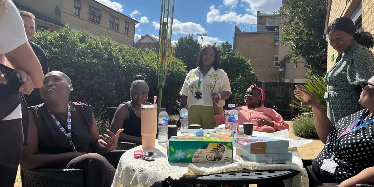 People are sat around a table in the garden smiling and sharing food.