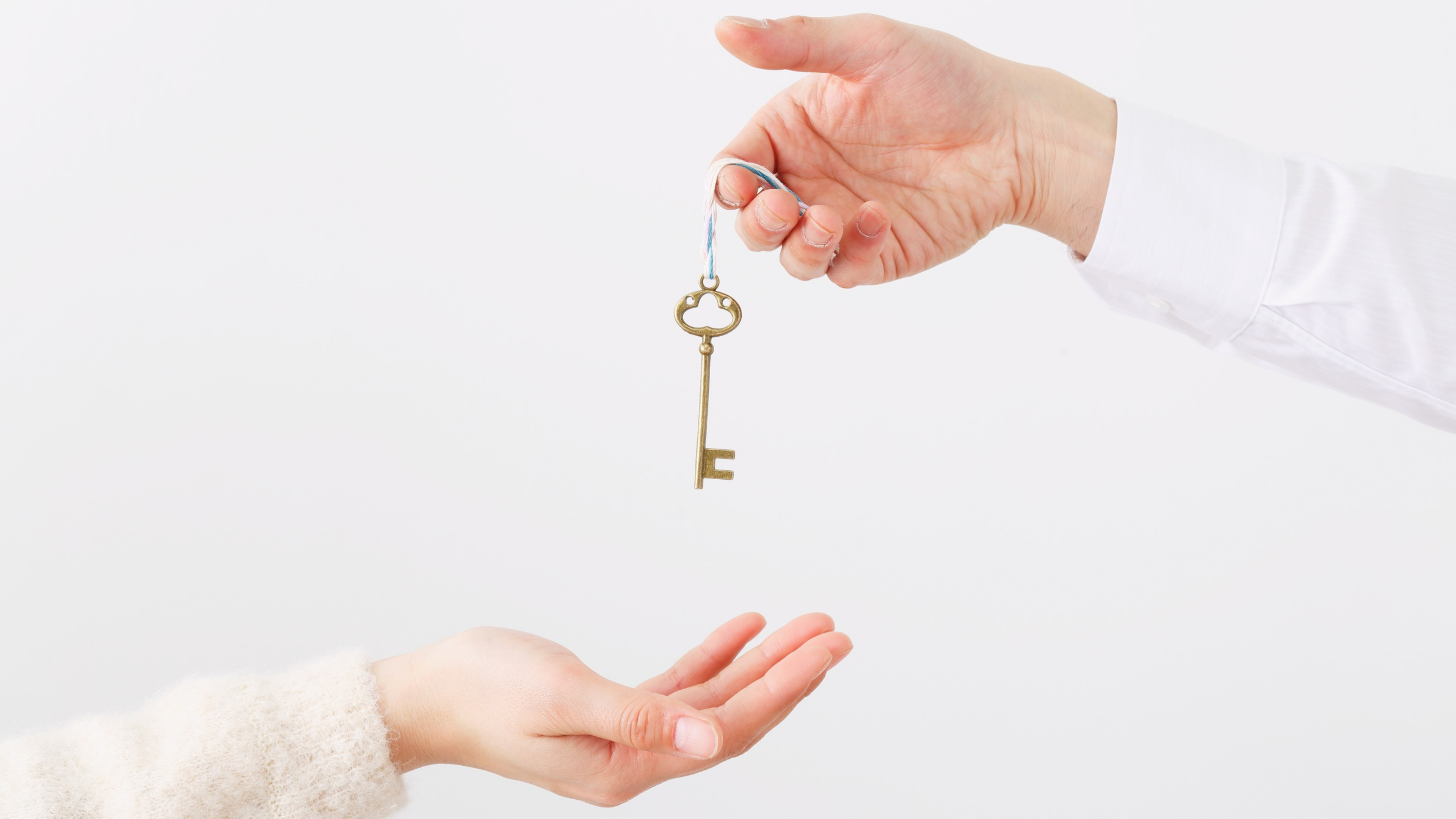 A hand holding a key, amount to give it to another hand.