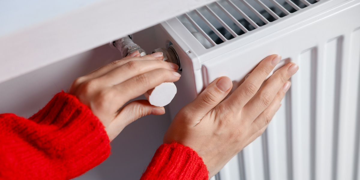 a woman wearing a red jumper is adjusting the temperature on her radiator.