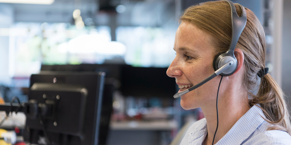 A smiling woman with a headset on takes a phone call. 
