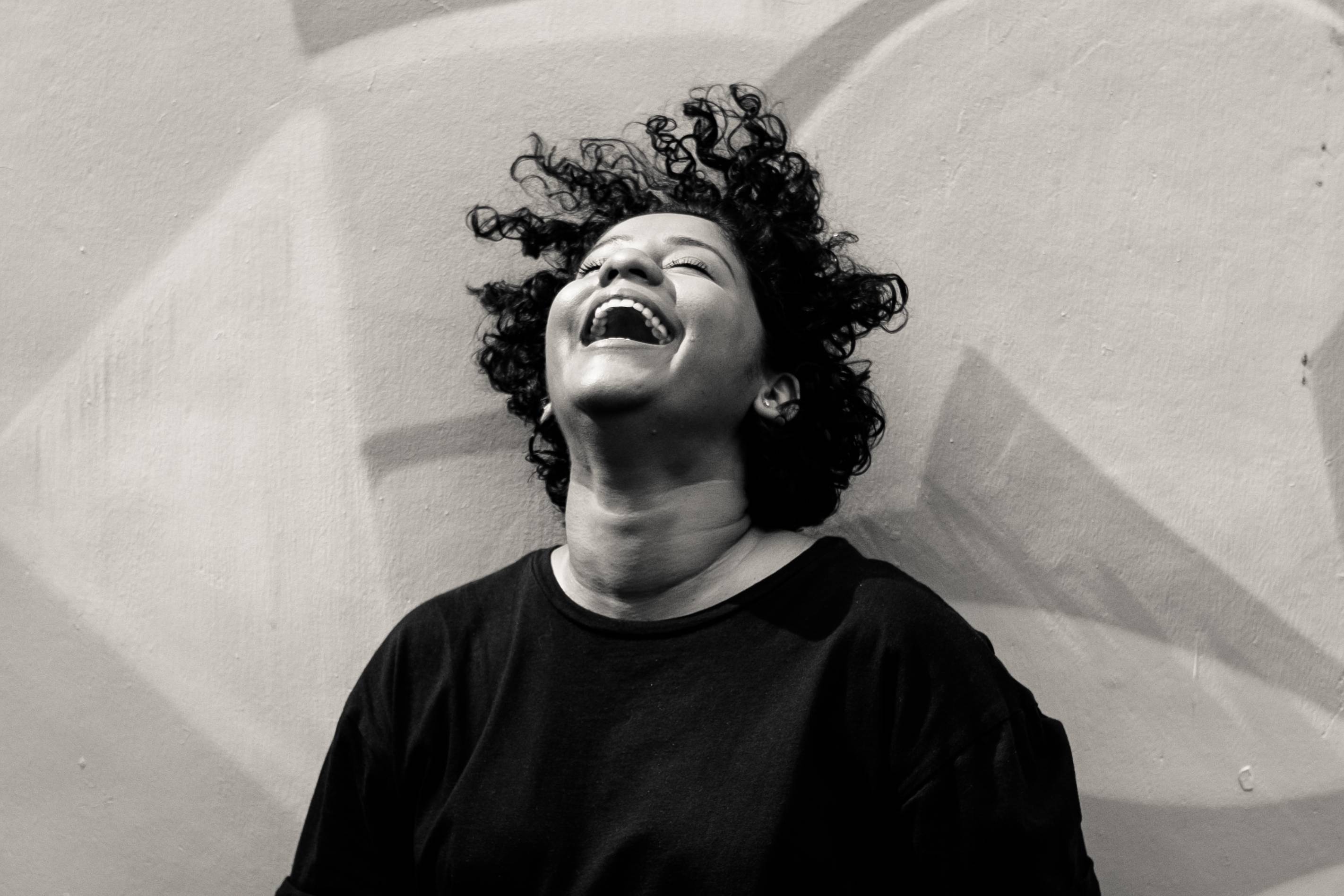 A woman laughing while sitting down against a patterned background.