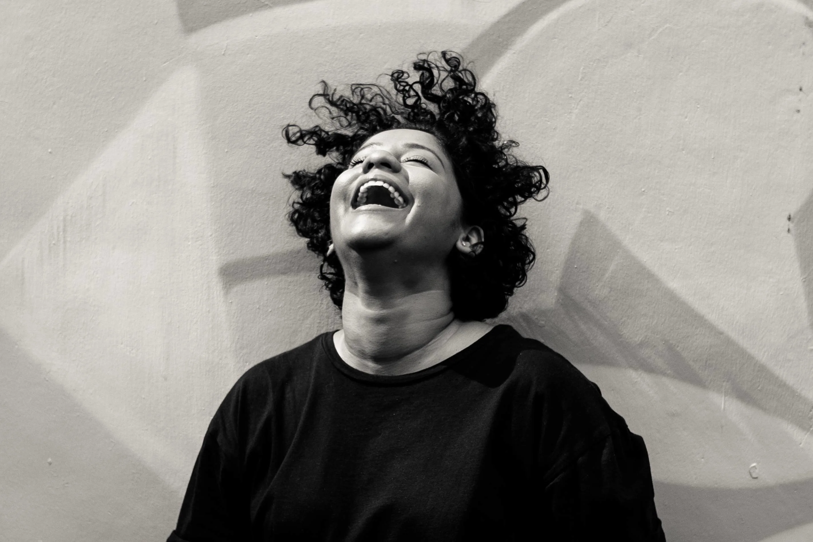 A woman laughing while sitting down against a patterned background.